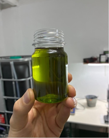 A sample jar of bright green early-harvest Picual olive oil held in a hand at the mill